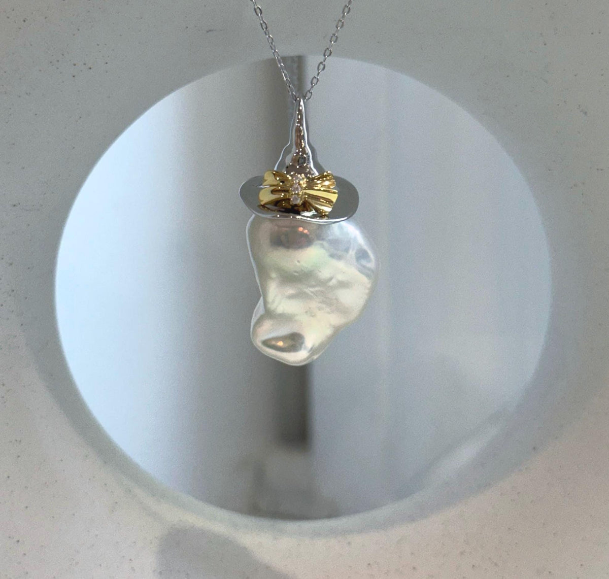 Mirror luster baroque pearl pendant displayed with genuine freshwater pearl earrings on a neutral stone background.