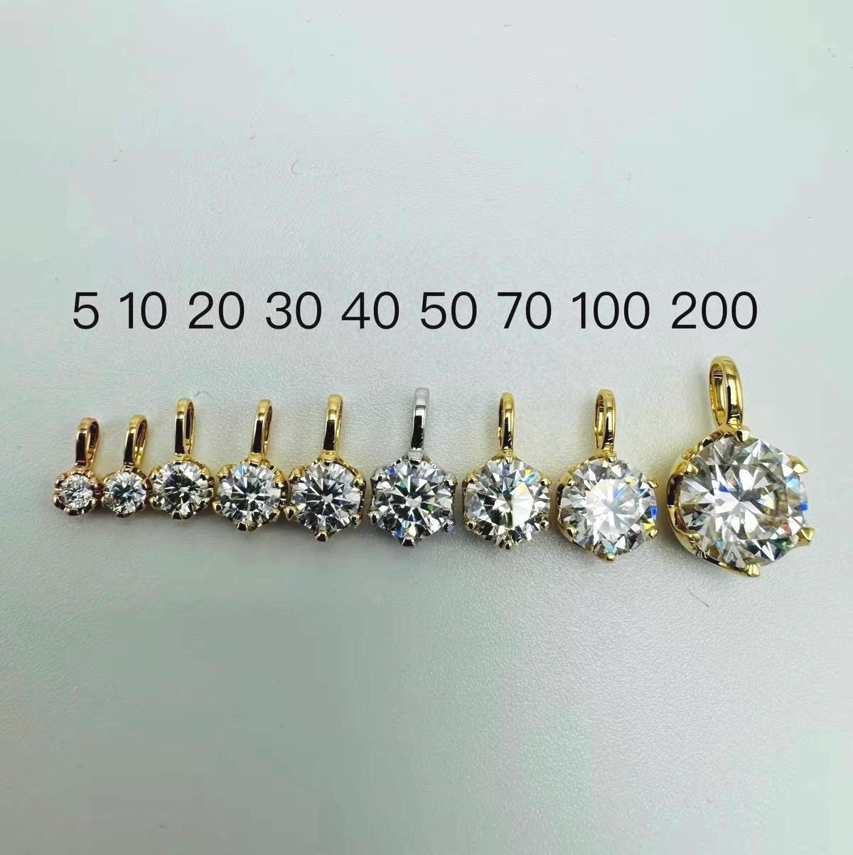 Moissanite solitaire pendant charms in 0.05 ct to 2.00 ct sizes shown beside ruler for size comparison.