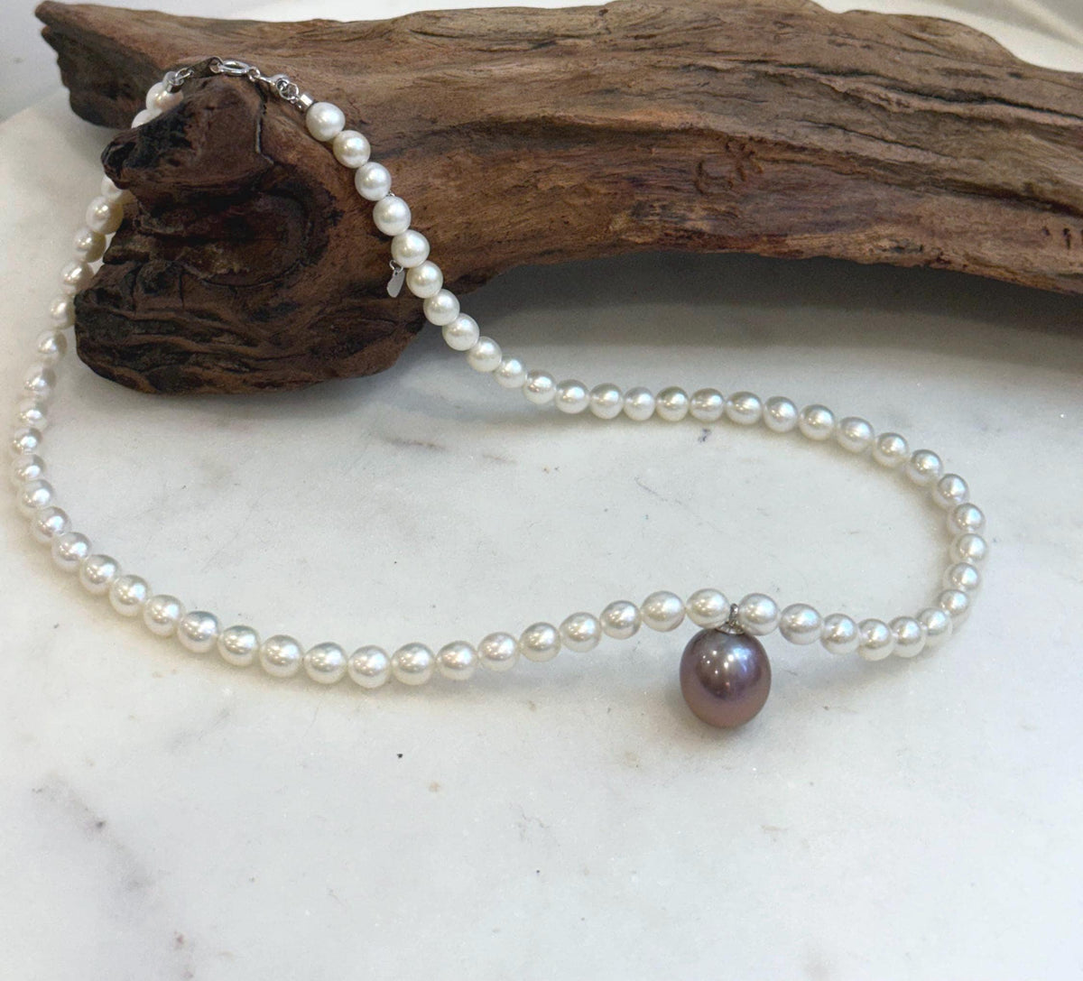 Elegant white pearl necklace featuring a large 12.9mm purple Edison pearl.