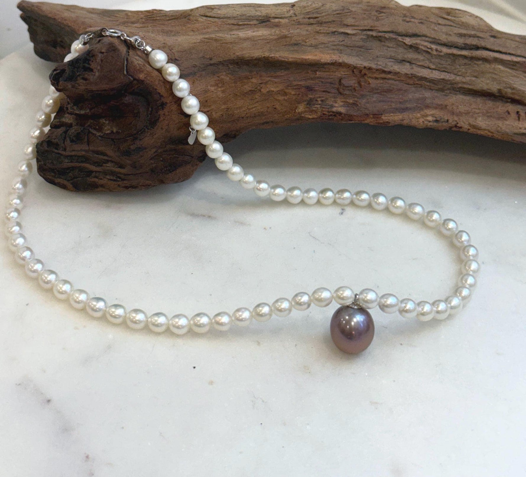 Elegant white pearl necklace featuring a large 12.9mm purple Edison pearl.