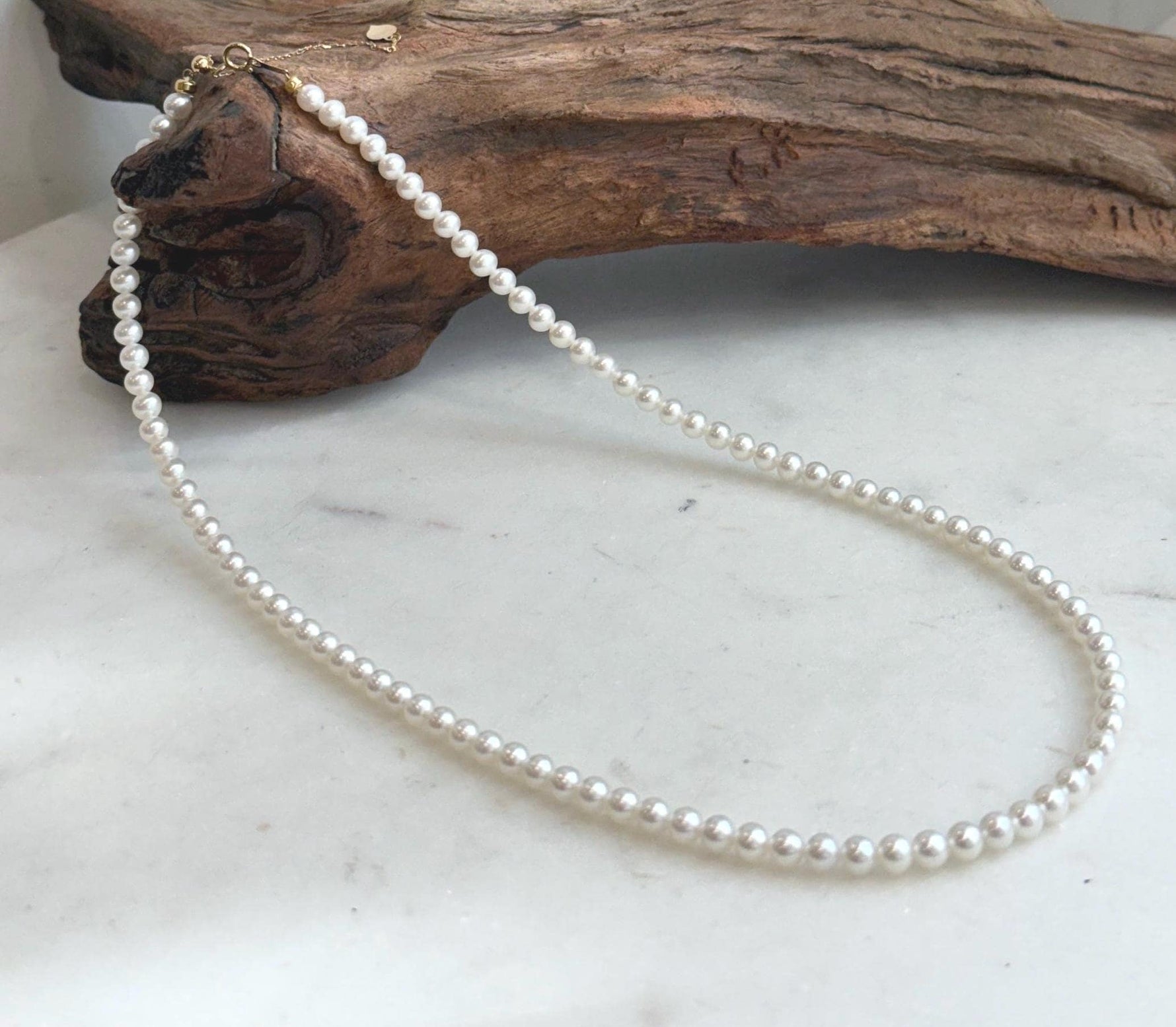 Elegant white small pearl strand showcasing bright mirror-like luster and solid 18K gold details.