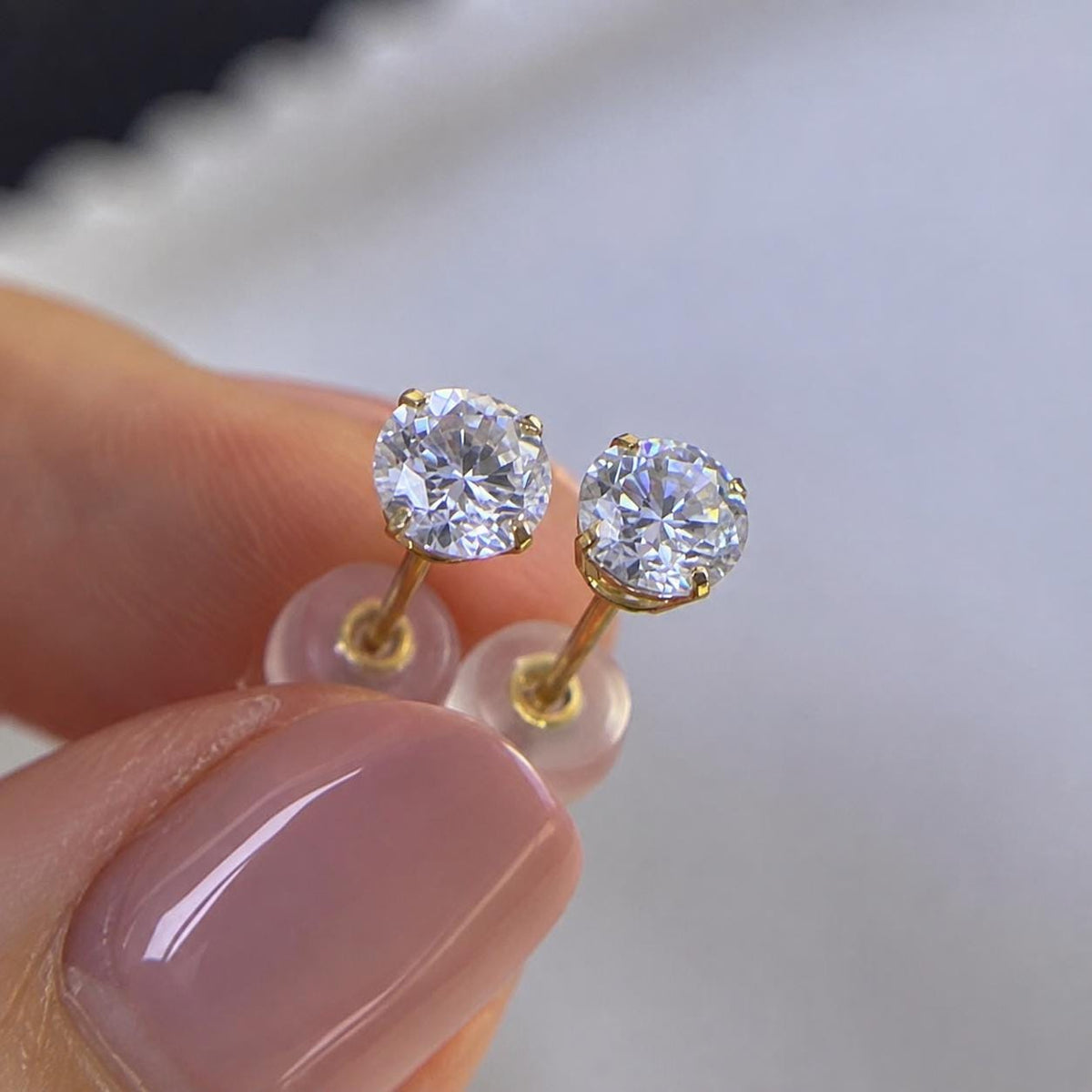 Solid 14K gold moissanite stud earrings featuring clear round brilliant-cut gemstones.