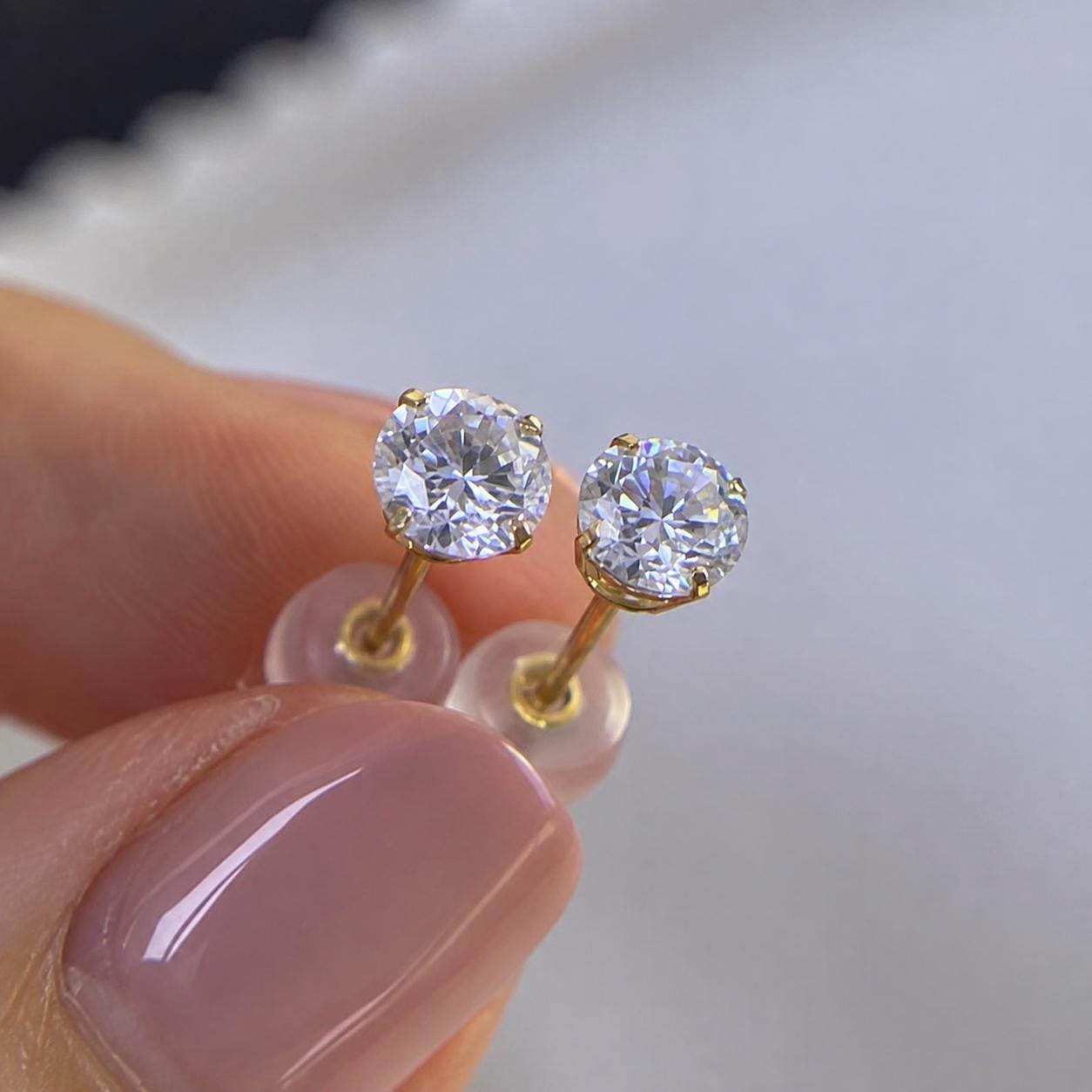 Solid 14K gold moissanite stud earrings featuring clear round brilliant-cut gemstones.