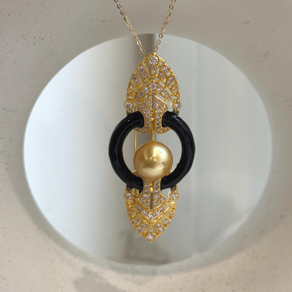 Two-in-one brooch and pendant featuring a lustrous South Sea golden pearl within a black circular frame.