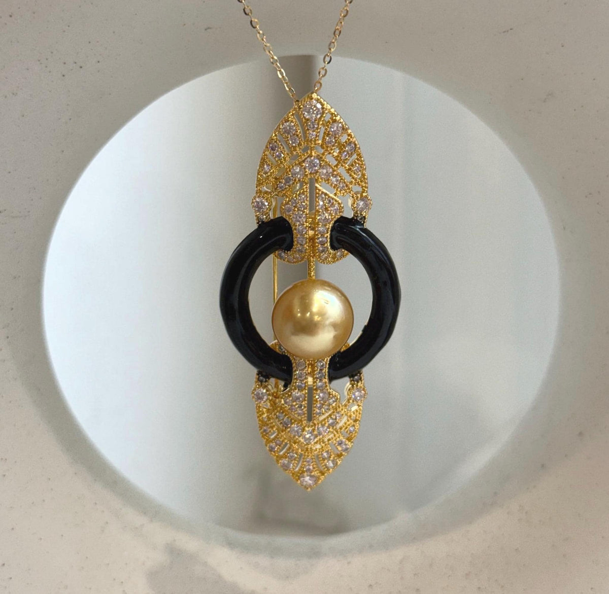South Sea golden pearl pendant suspended from a delicate gold tone chain on a cream display.