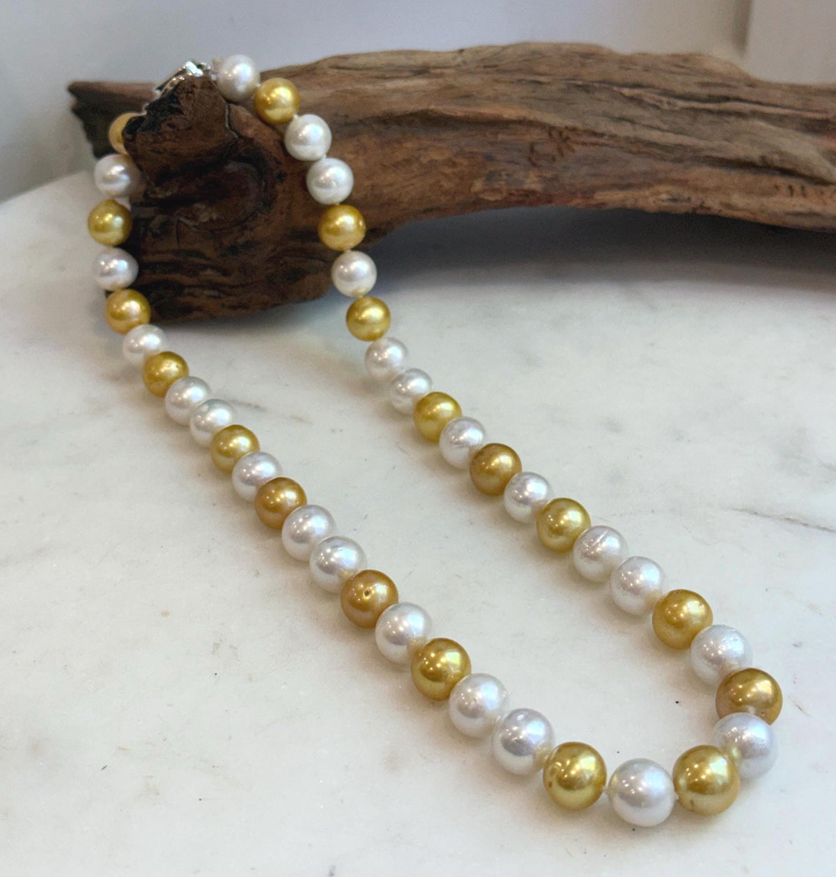Close view of alternating white and golden freshwater Edison pearls with glossy luster.