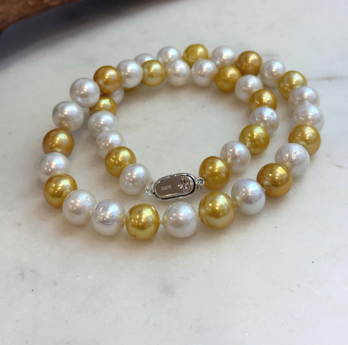 White and gold pearl necklace photographed beside a piece of natural driftwood.