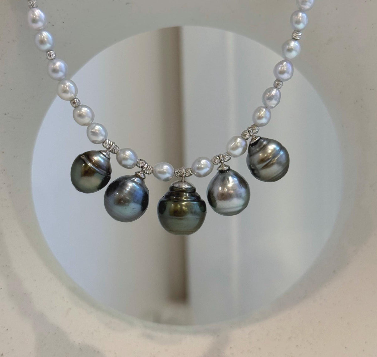 Side view of the white pearl strand and Tahitian drops on a jewelry display.