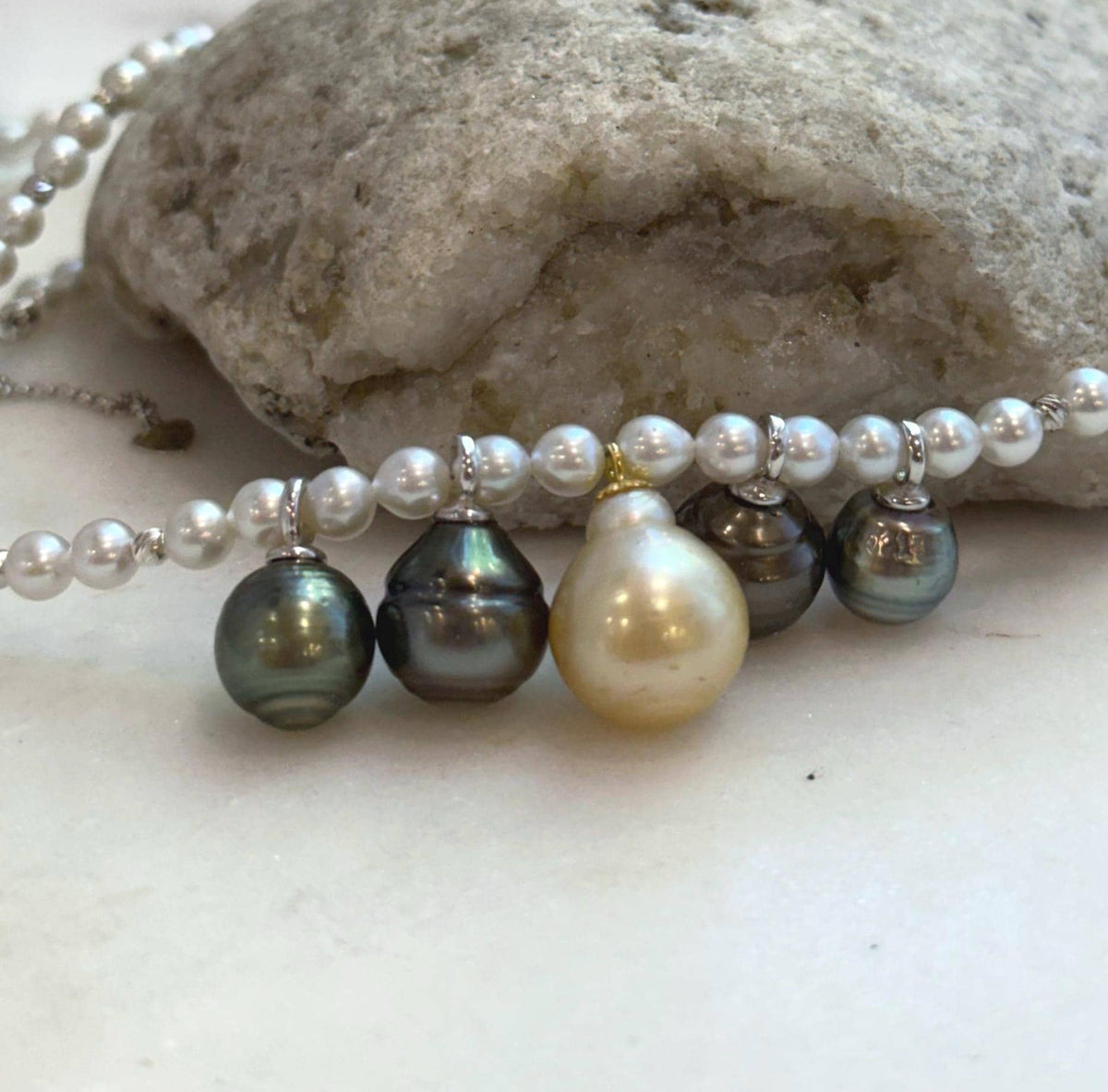 Pearl necklace arranged on a white surface beside natural driftwood.