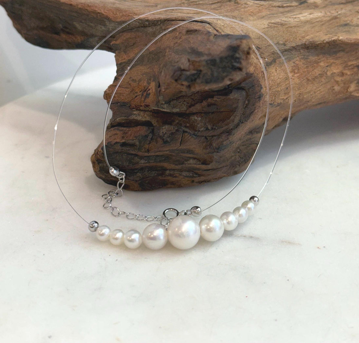 Floating pearl necklace with a large central white pearl and smaller pearls arranged symmetrically on each side.