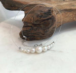Floating pearl necklace with a large central white pearl and smaller pearls arranged symmetrically on each side.