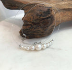 White pearl necklace laid flat on a pale surface, showing its clear nylon cord and extension chain.