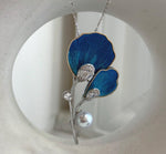 Akoya pearl suspended below a pair of deep blue flower petals.