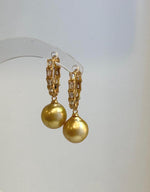 Close-up of lustrous golden South Sea pearls on elegant gold-tone hoop earrings.