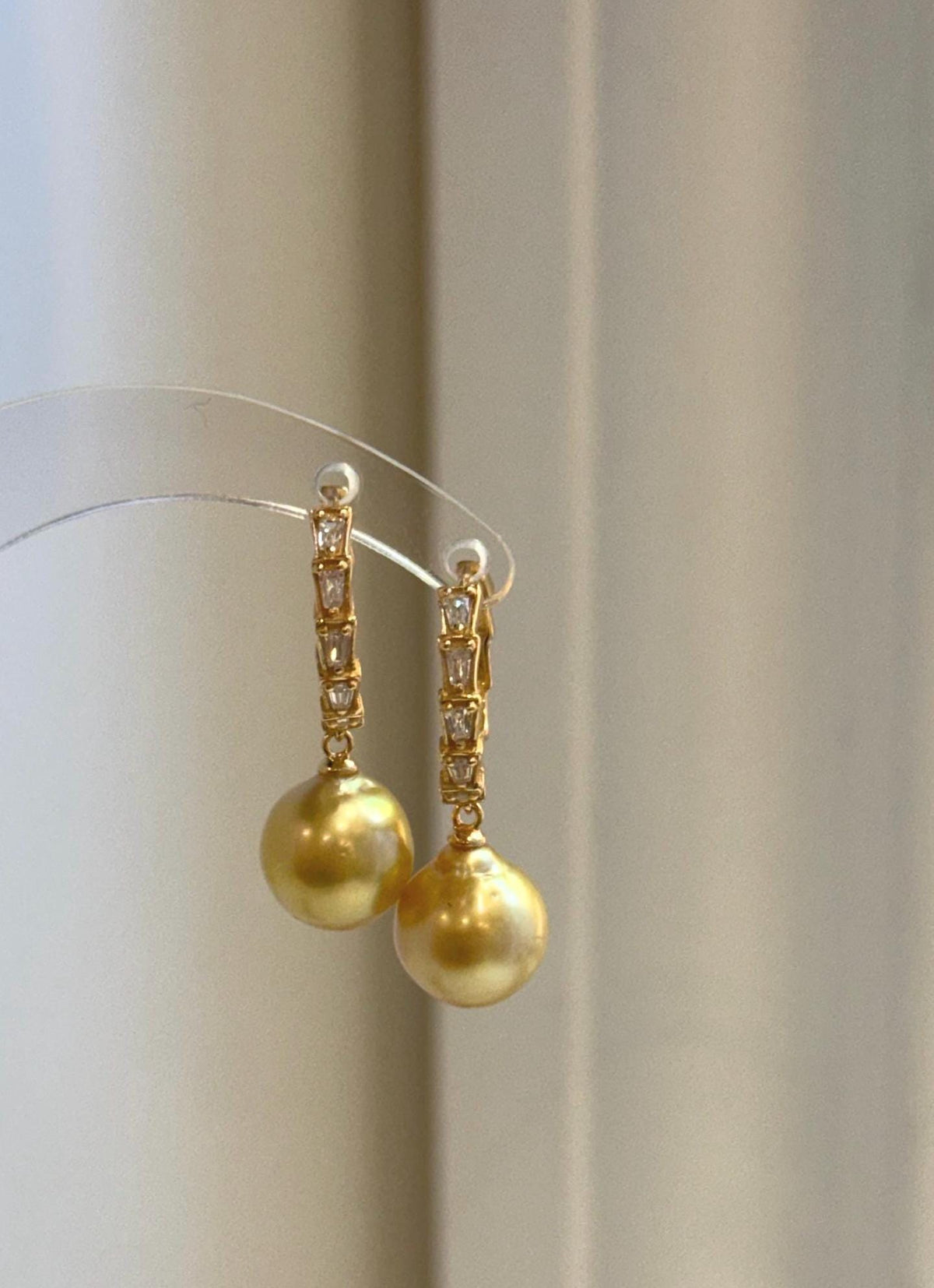 Golden pearl drop earrings combining South Sea pearls with curved gold-tone hoops.