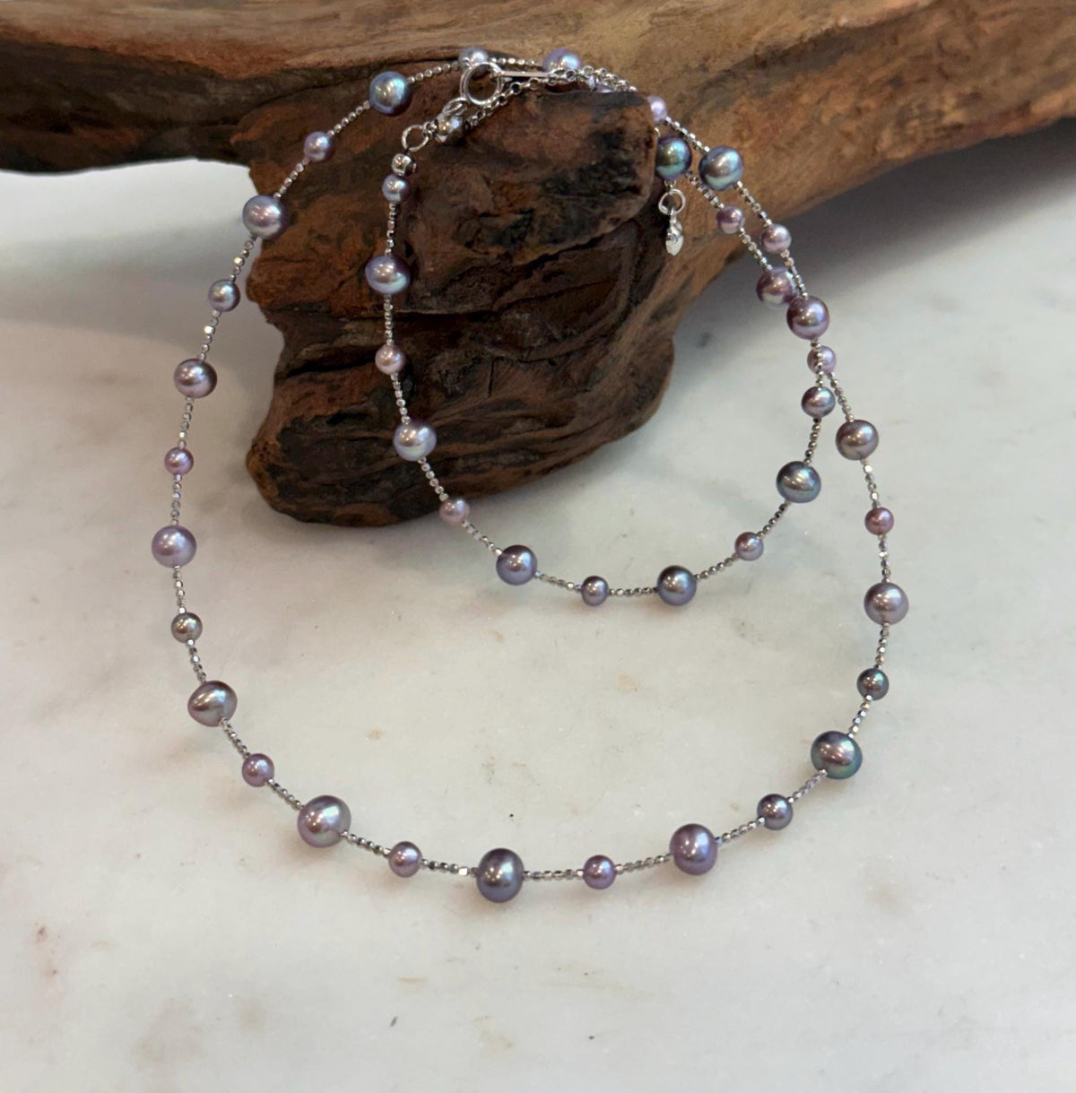 Purple and pink pearls arranged at intervals along a fine sterling silver necklace