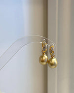 Front view of two golden pearl drop earrings with sparkling accents on the hoops.