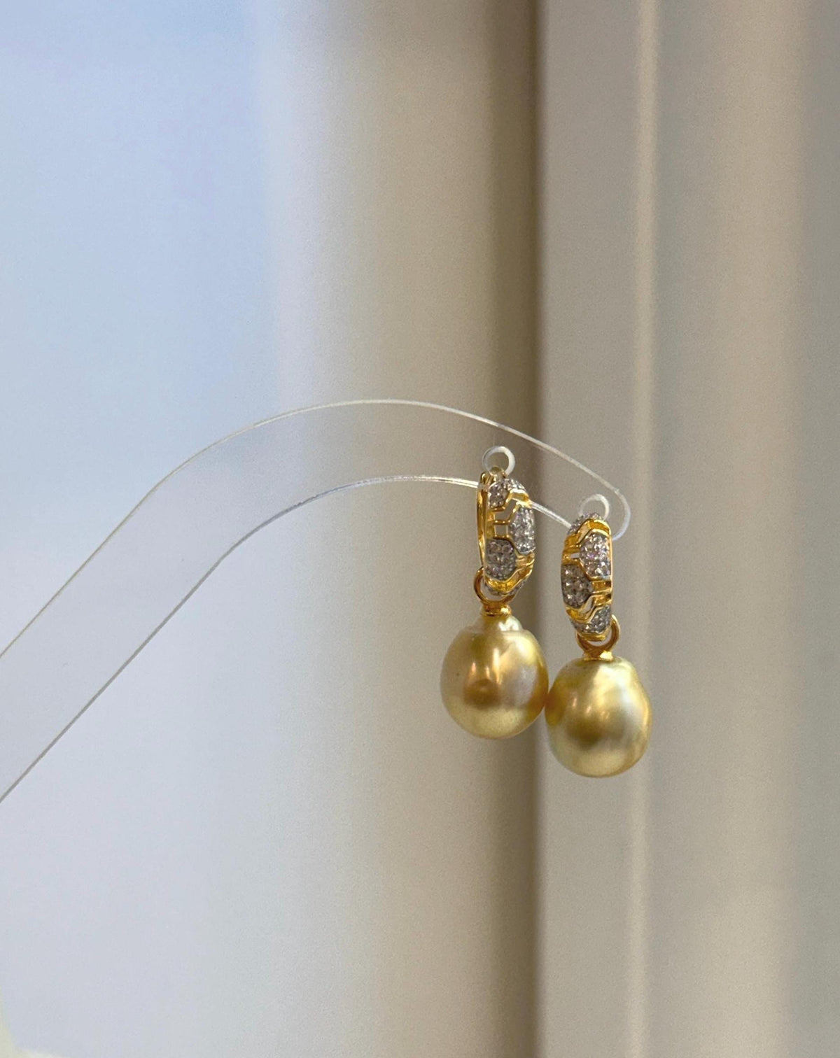 Front view of two golden pearl drop earrings with sparkling accents on the hoops.