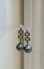 Front view of Tahitian pearl earrings suspended from geometric sterling silver designs.