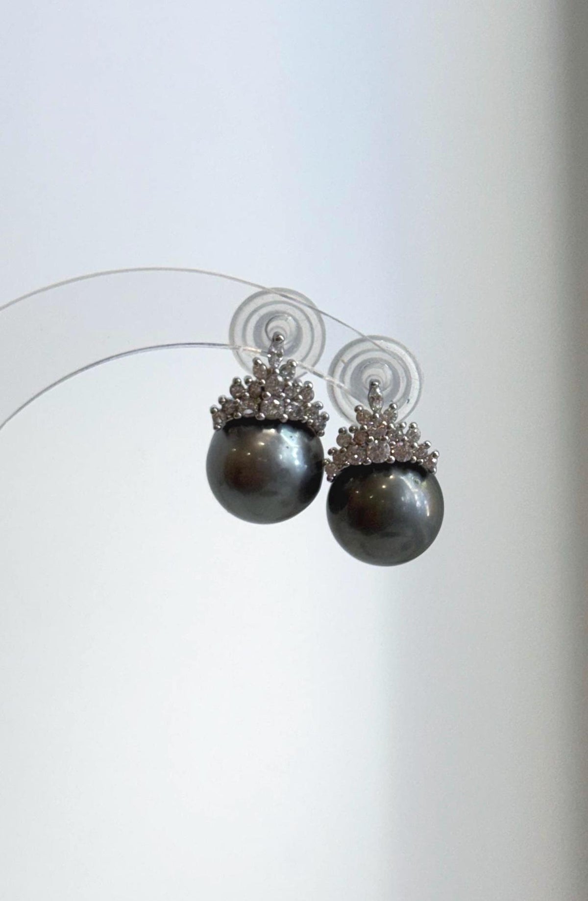 Tahitian pearl crown earrings displayed on a clear stand.