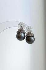 Tahitian pearl crown earrings displayed on a clear stand.