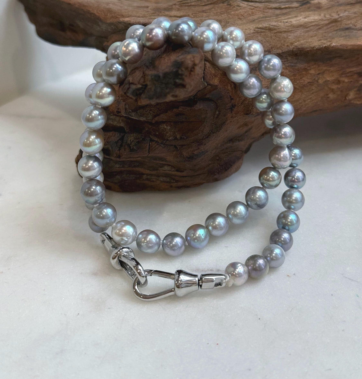 Blue grey saltwater pearl necklace coiled on a white surface with an S925 silver clasp.
