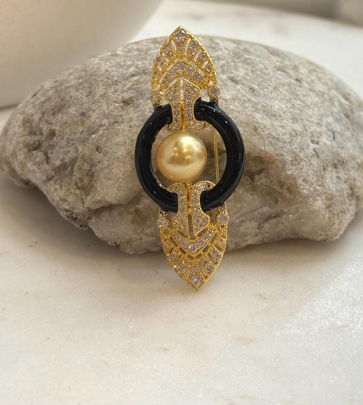 Golden South Sea pearl framed by two glossy black arcs between decorative gold tone pointed ends.