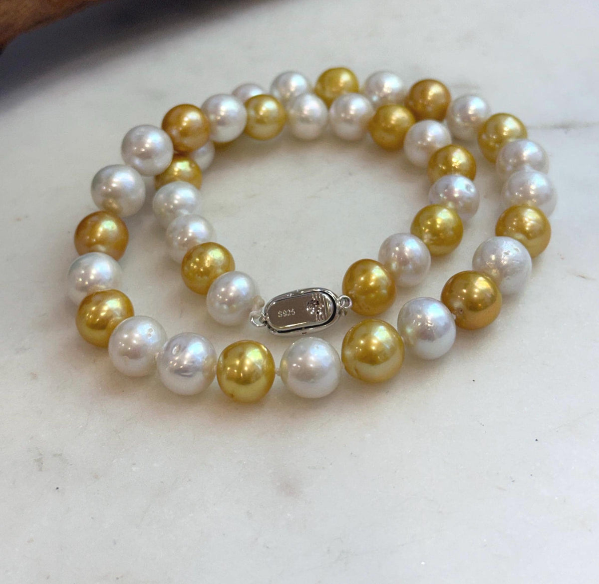 White and golden Edison pearl necklace arranged in a double loop on a white surface.