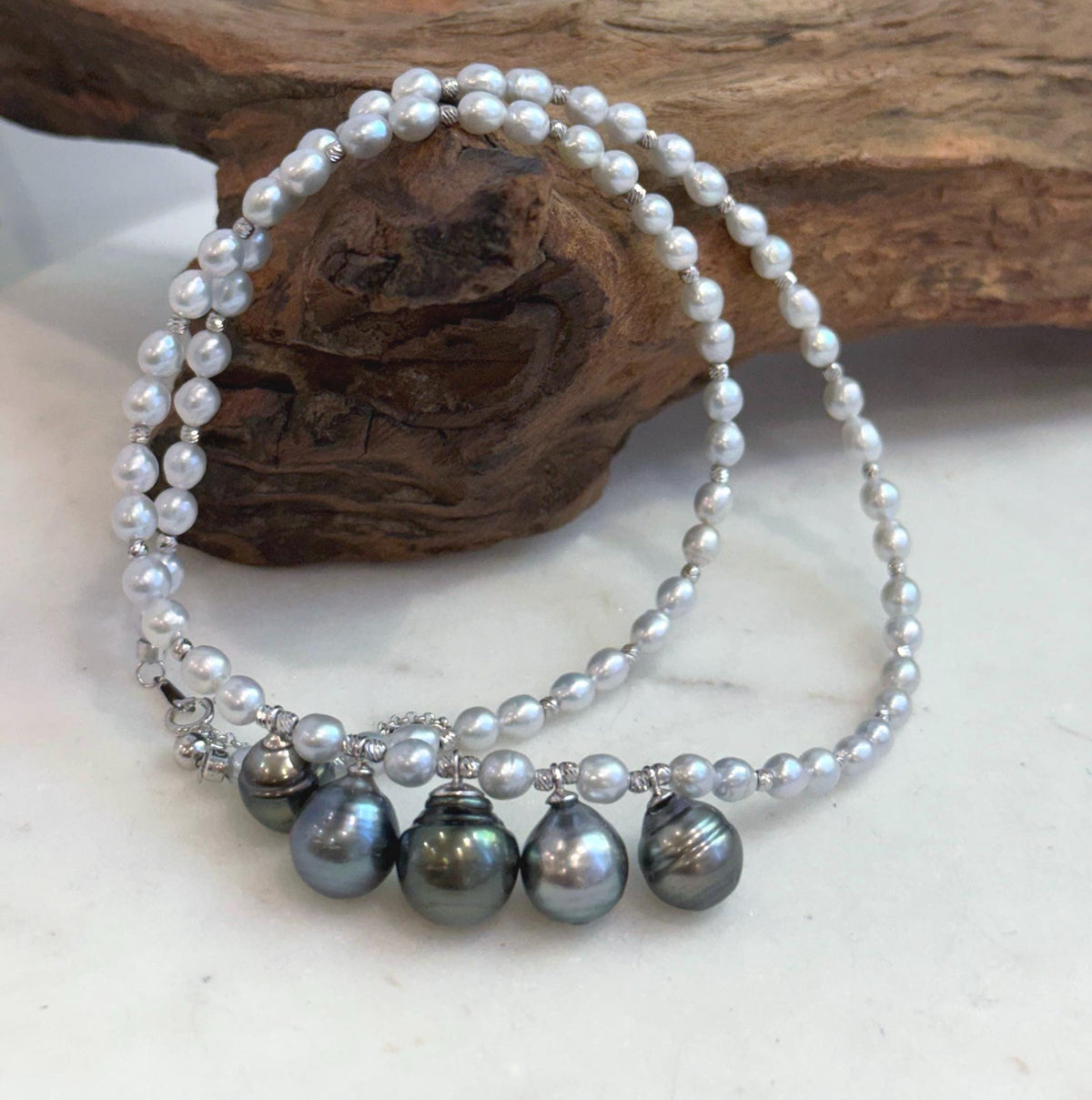 Five Tahitian pearl drops in platinum, gray and peacock tones hanging from a white pearl strand.