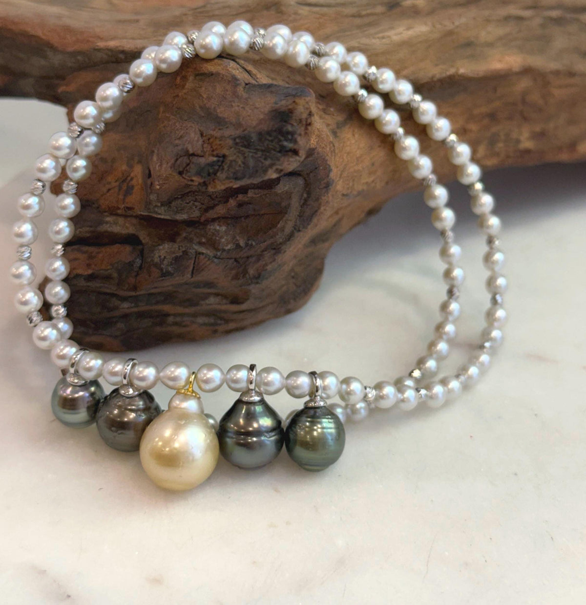 Five South Sea pearl drops with platinum and golden tones displayed on a necklace stand.