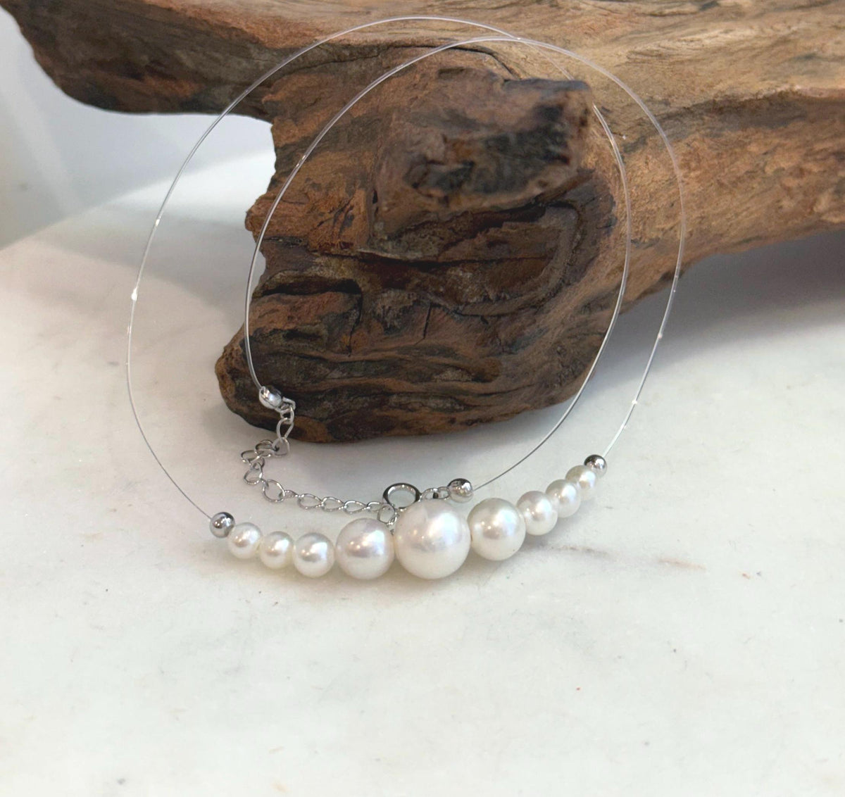 Graduated white pearls with reflective luster, framed by small silver-tone beads on a transparent cord.
