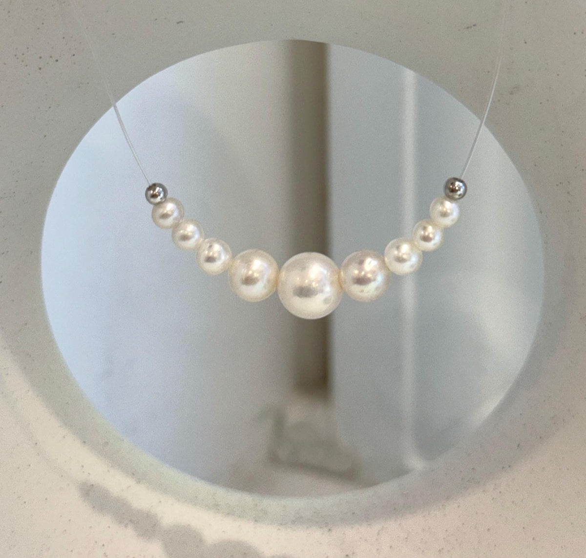 Minimalist floating pearl necklace displayed against a cream stand with a circular opening.