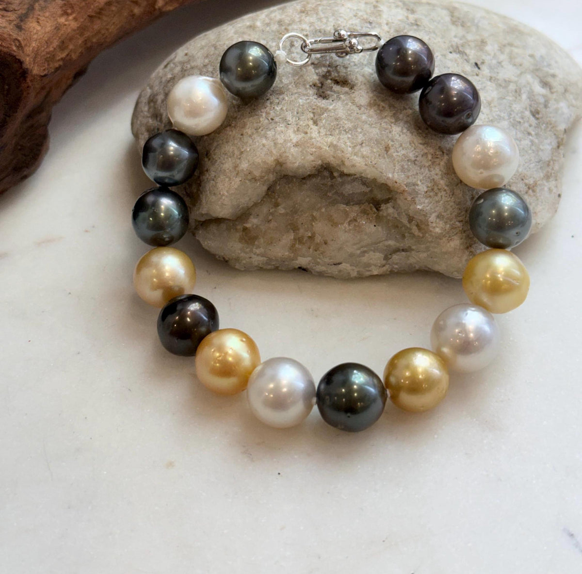 Golden, white and dark ocean pearls displayed on driftwood.