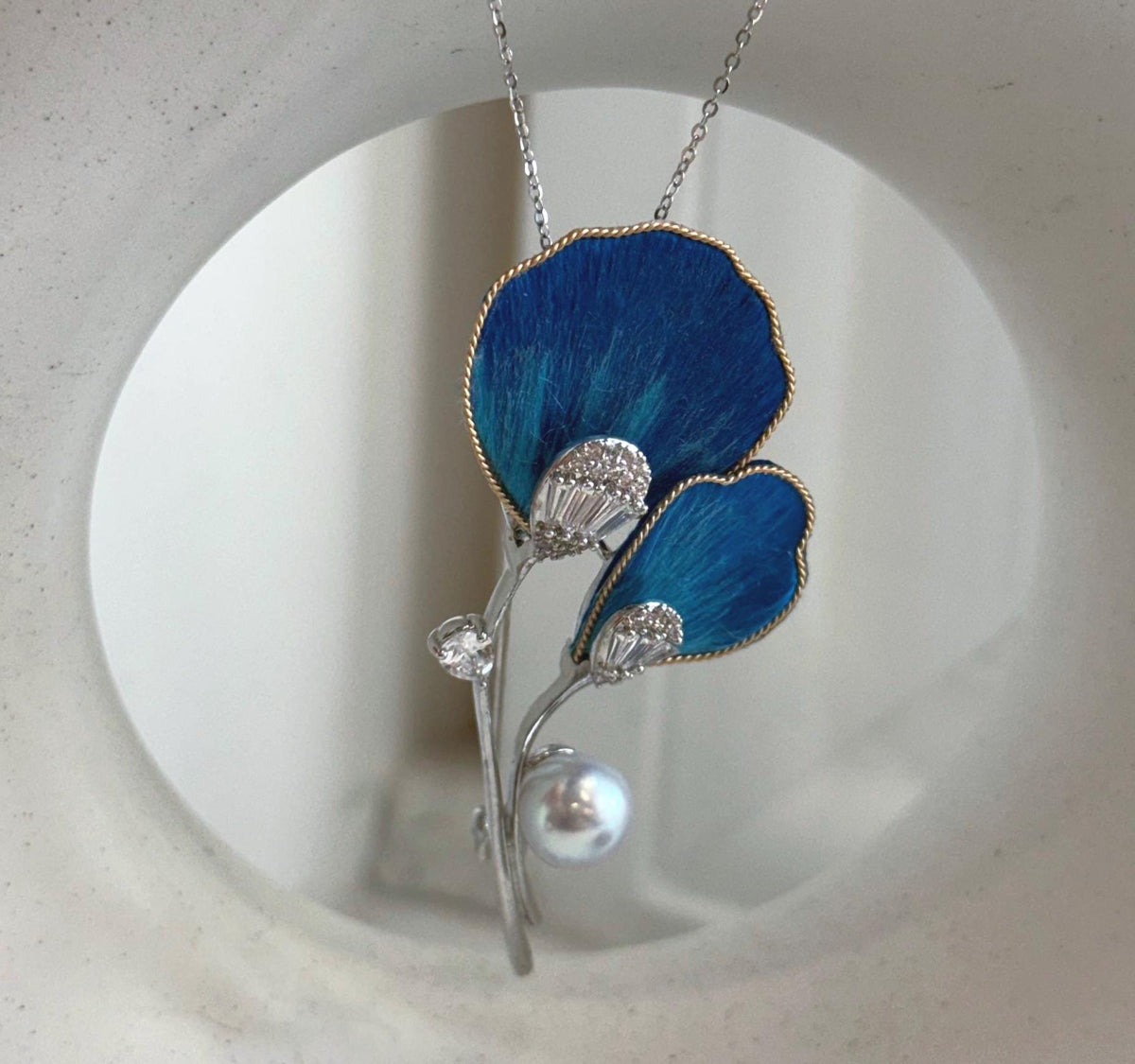 Genuine saltwater Akoya pearl paired with textured blue petals and gold-tone edges.