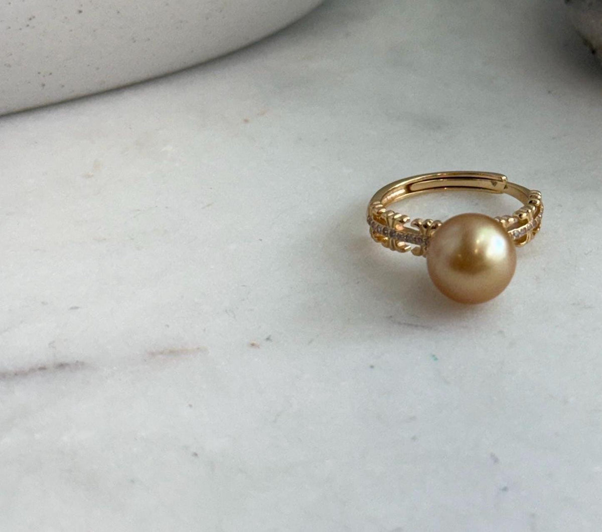 Adjustable pearl ring with a layered gold-tone band and sparkling accents.