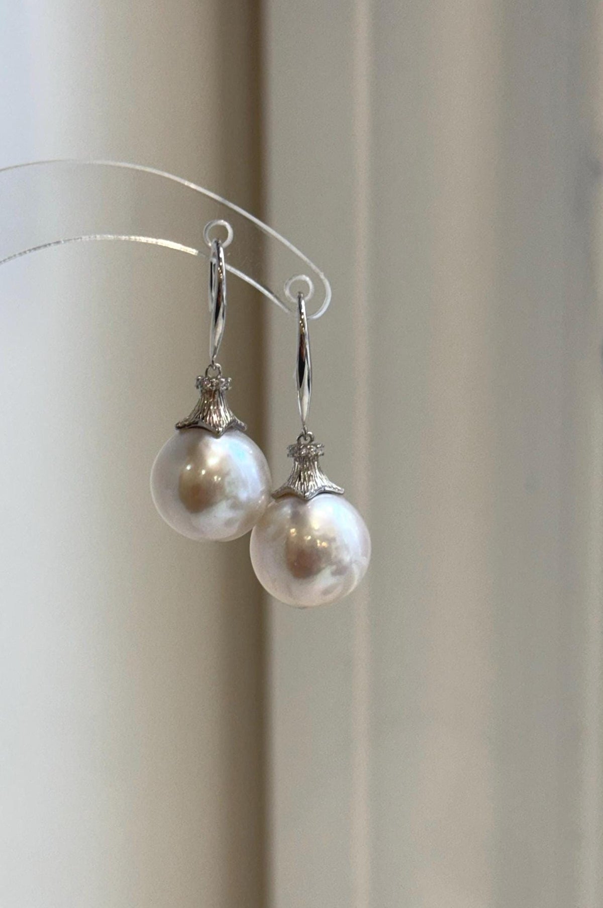 Pair of white Edison pearl earrings hanging from a clear display stand.