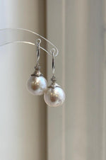 Pair of white Edison pearl earrings hanging from a clear display stand.