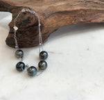 Tahitian pearl bracelet displayed on a pale stone surface beside natural driftwood.