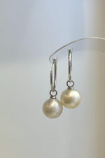 Round white pearl drops displayed on polished silver hoops