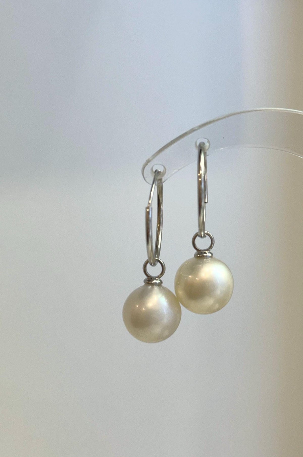 Round white pearl drops displayed on polished silver hoops