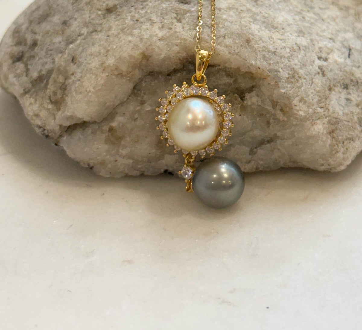 Golden South Sea pearl framed by clear sparkling stones above a platinum gray Tahitian pearl.