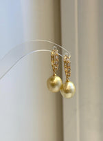 A pair of golden pearl earrings suspended from sparkling hoop settings.