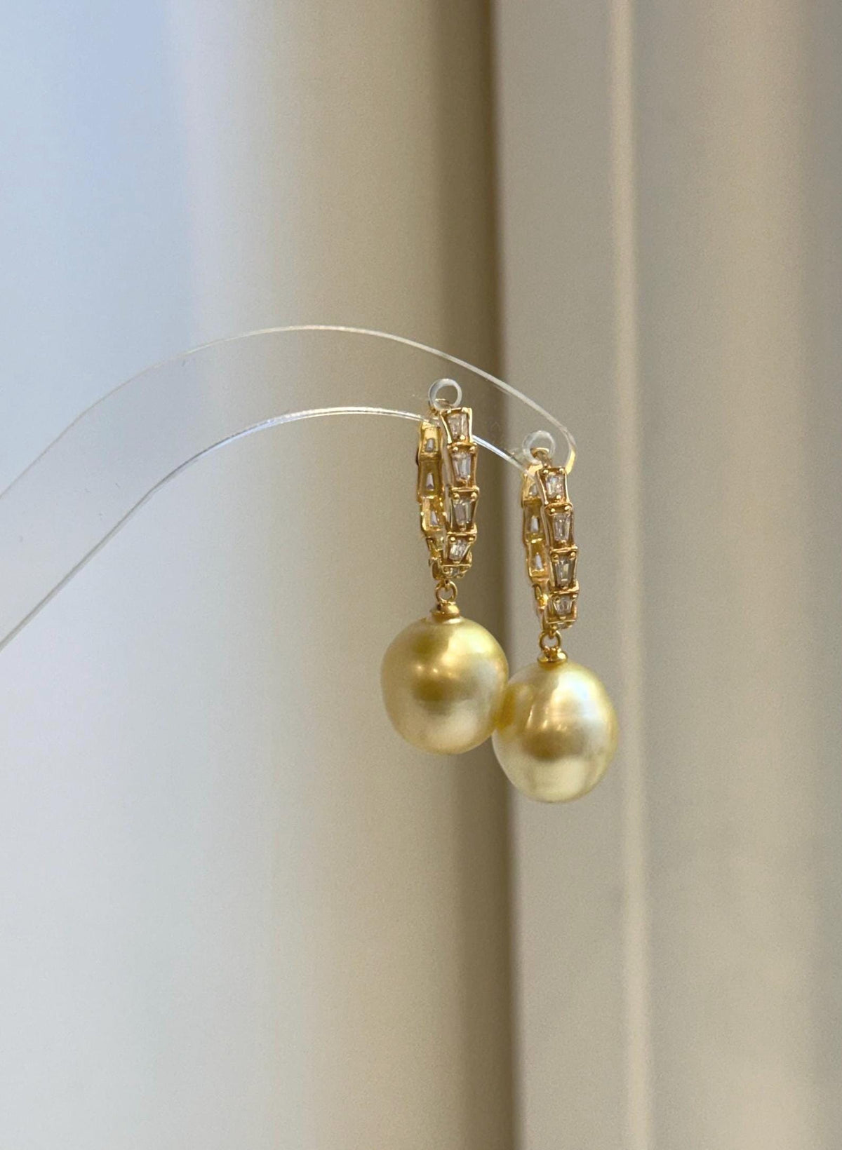 A pair of golden pearl earrings suspended from sparkling hoop settings.