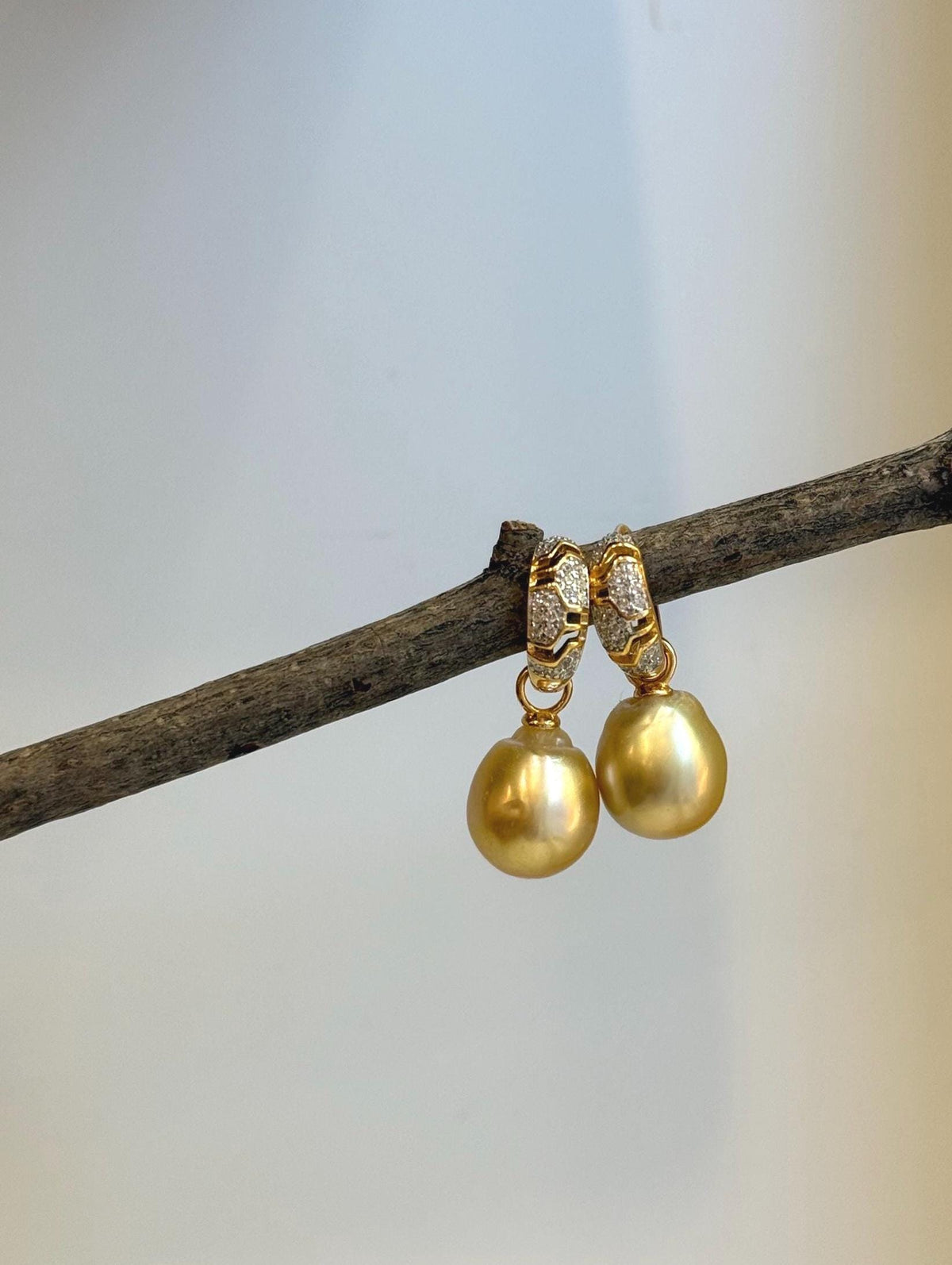 Pair of golden South Sea pearl earrings suspended from crystal-accented gold-tone hoops.