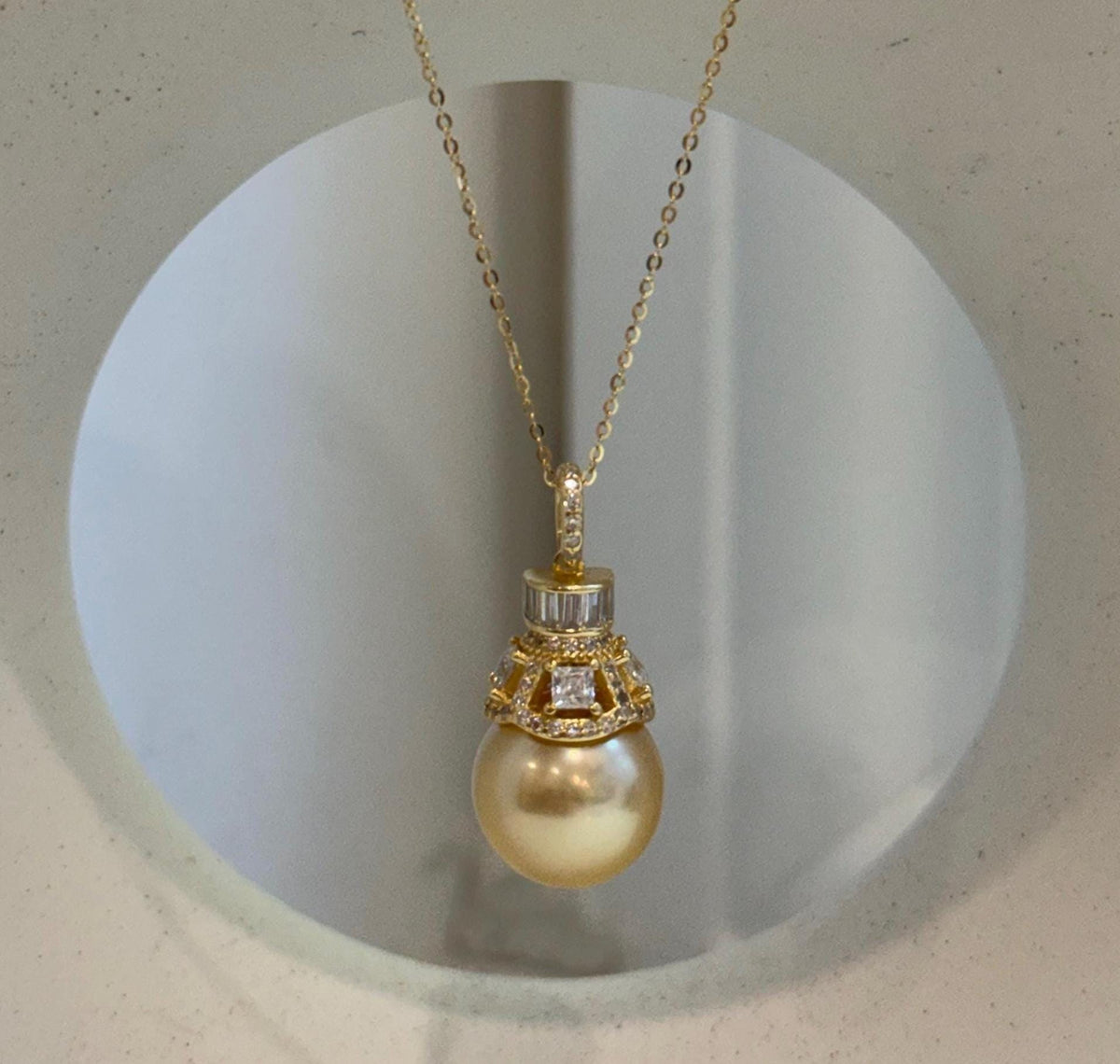 Large golden pearl suspended beneath a sparkling crystal-accented bail.