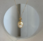 Golden drop pearl hanging from a delicate gold-tone necklace chain.