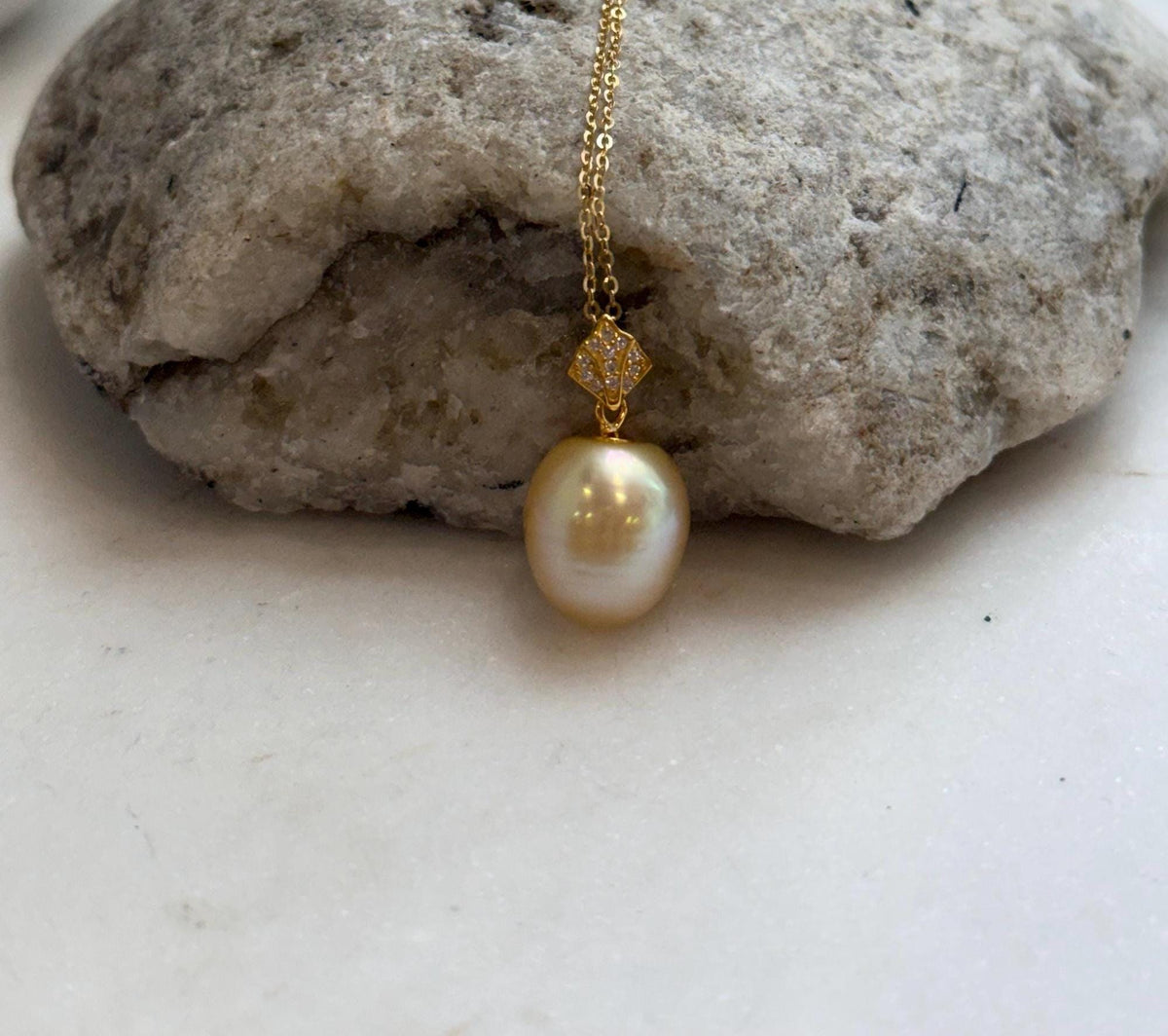Front view of the golden pearl beneath its sparkling geometric bail.