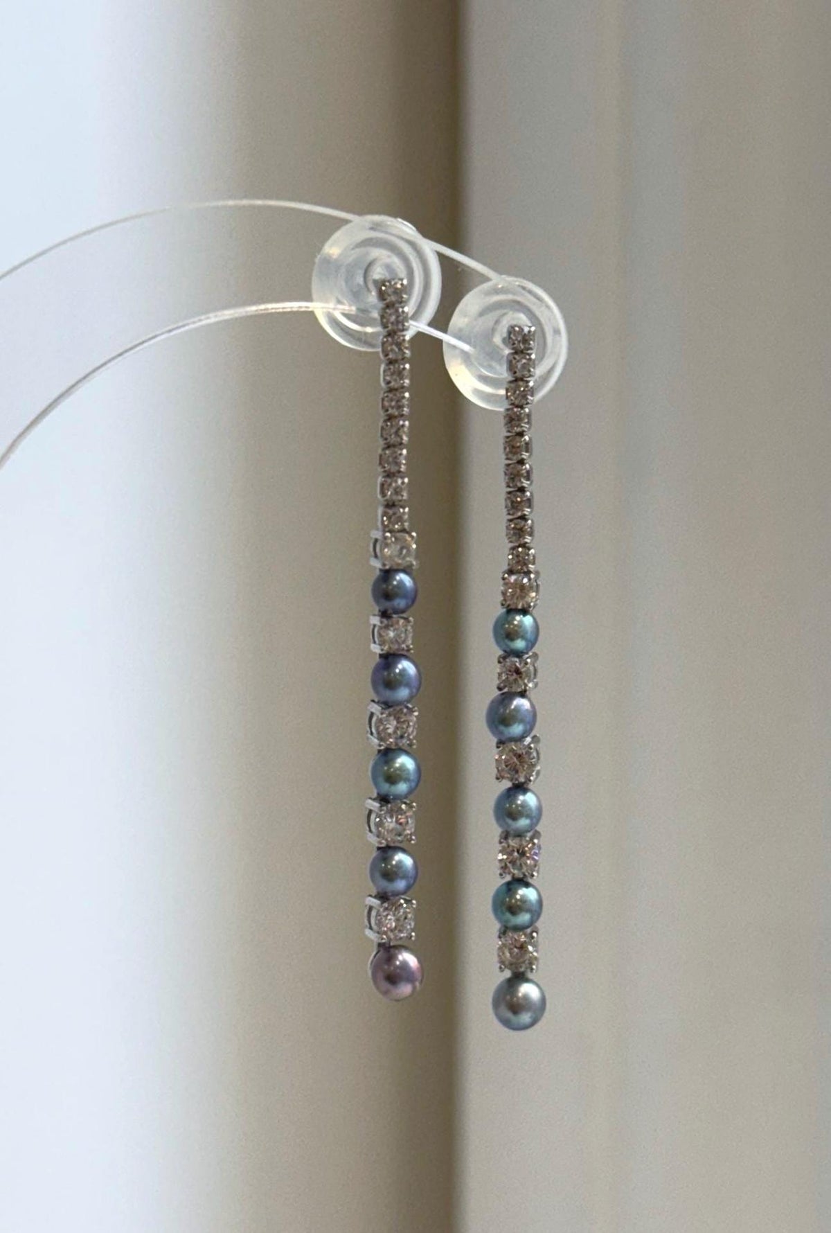 Long pearl earrings displayed on a clear jewelry stand.