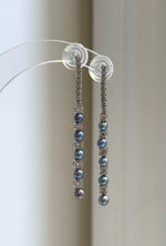 Long pearl earrings displayed on a clear jewelry stand.