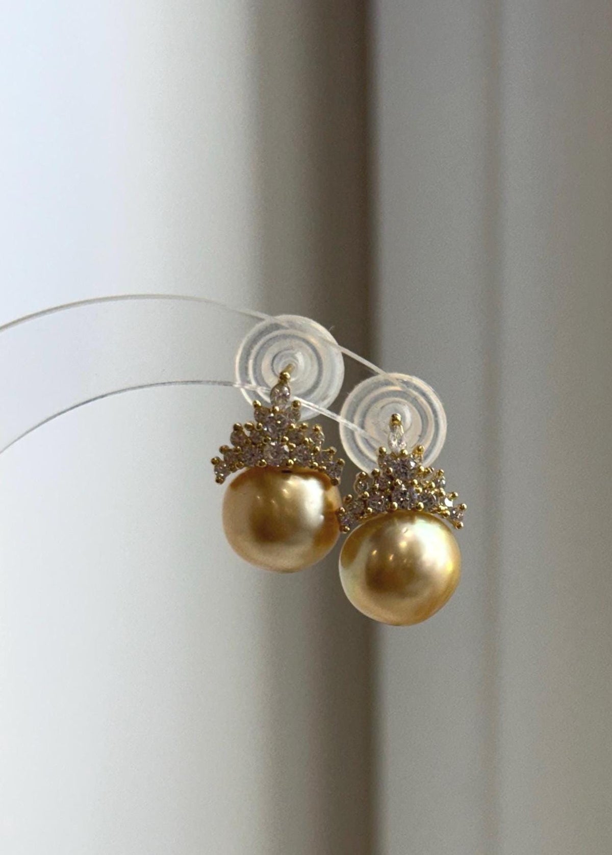 Golden pearl stud earrings with crystal-accented crown details.